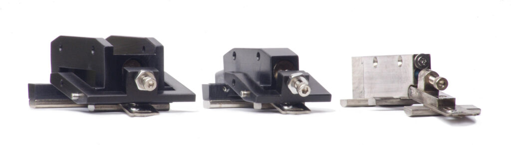 three metal measuring heads, each with a pivot point and an adjustment screw visible. on the left is the L-CAT which is made of black hard-coated aluminum and nickel-plated steel; it is the largest of the three; in the middle is the S-CAT which is similar to the L-CAT head but smaller, and on the right is the mu-CAT head which is made of nickel-plated steel and smaller than the S-CAT head.